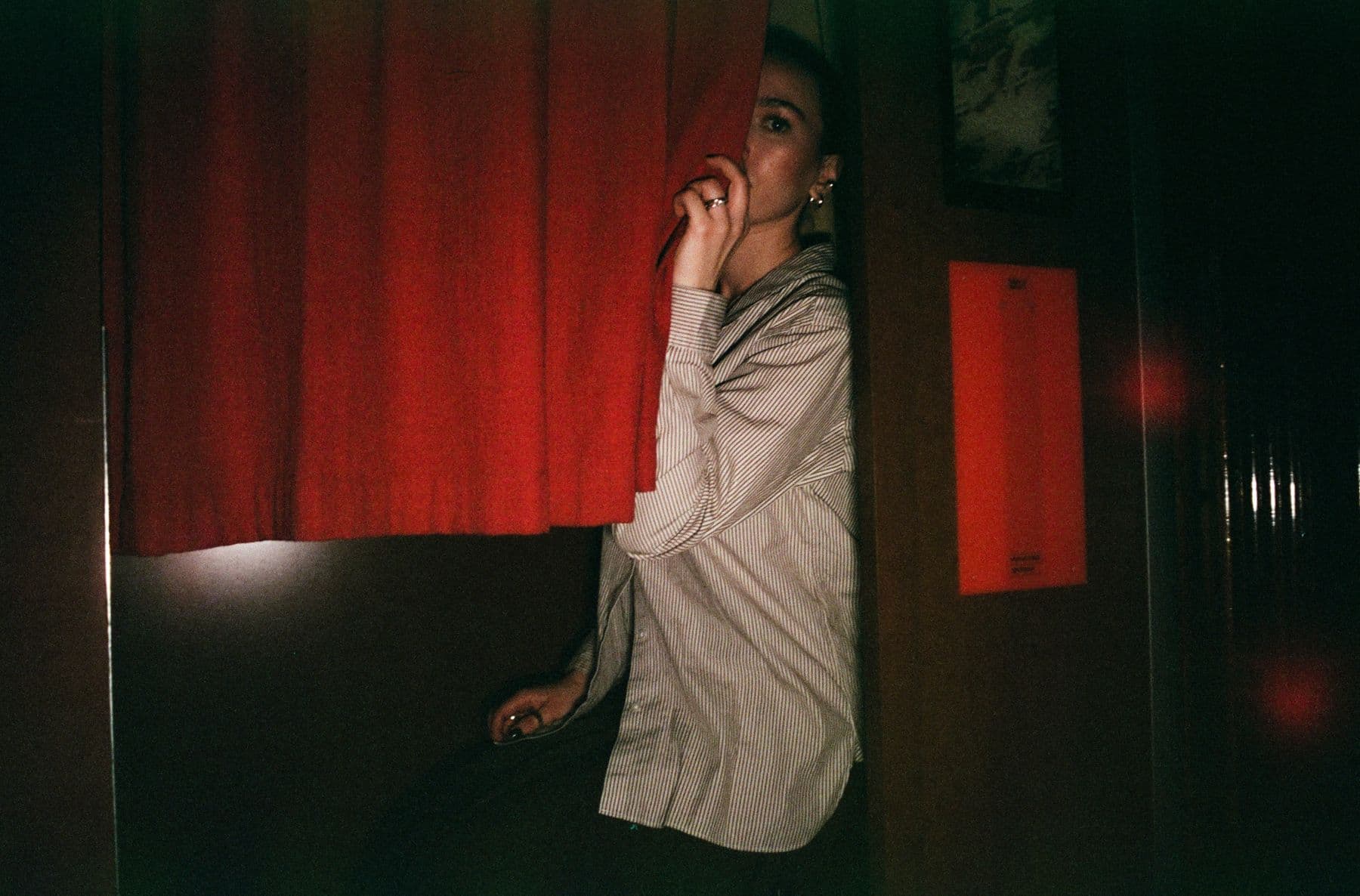 A member glancing back from behind the red curtain of a photo booth
